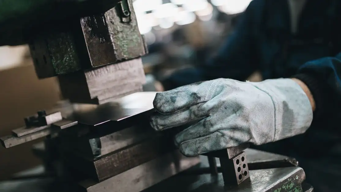 Un obrero trabajando una pieza de metal, con guantes, como parte de un proceso de metalurgia.